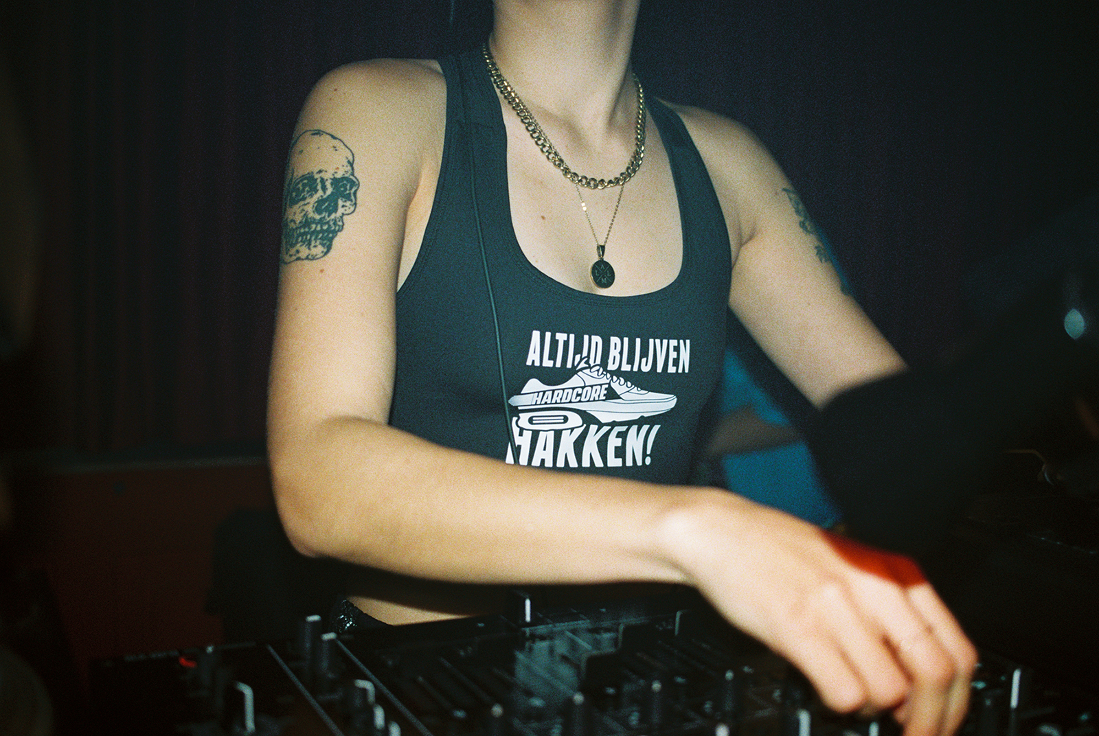 This photo shows a person behind a turntable. Of the person, you can only see the upper body, but not the head. Her shirt reads "Altijd blijven hakken!".